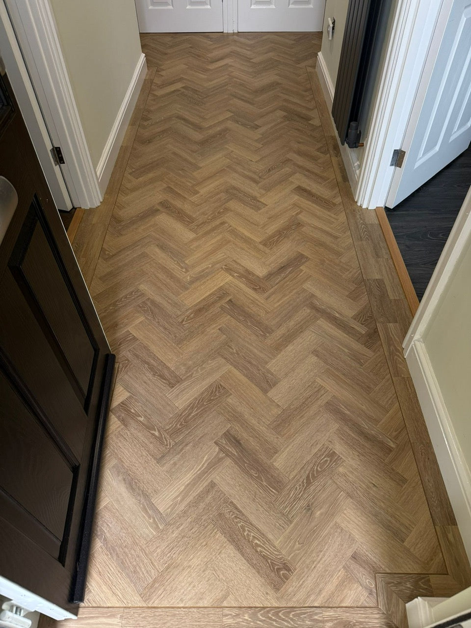 Wooden floor with herringbone pattern in a room with white walls and doors.