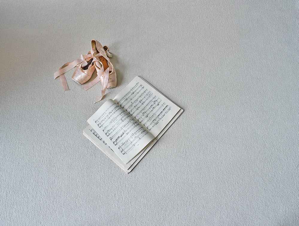Open book with music notes on a light gray surface, accompanied by ballet shoes.