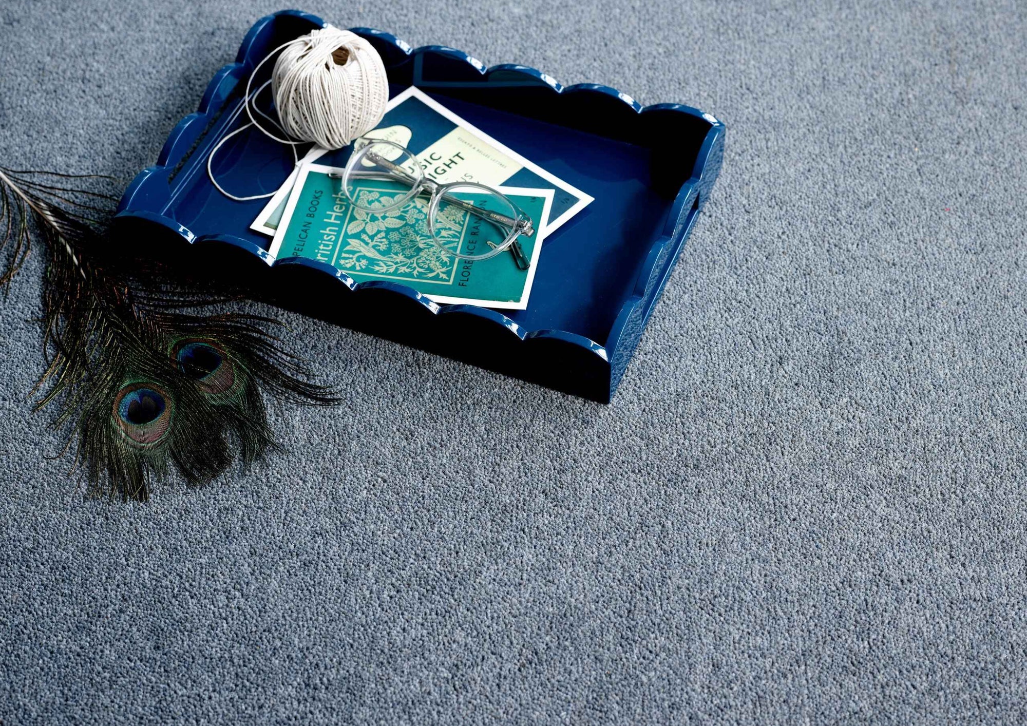 Blue decorative tray with peacock feather, yarn, and cards on a gray carpet
