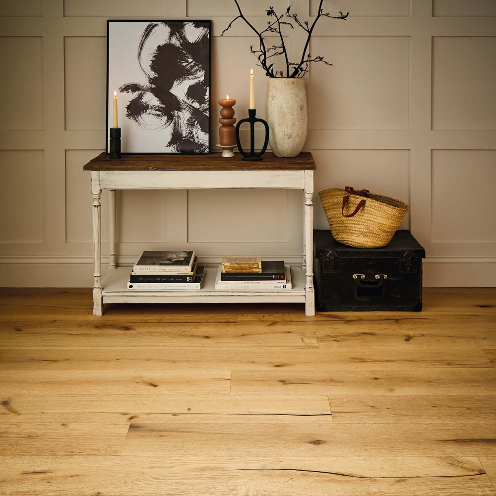Light oak hardwood flooring with visible wood grain and knots, shown in a styled room setting with a white console table, decorative items, and a paneled beige wall.